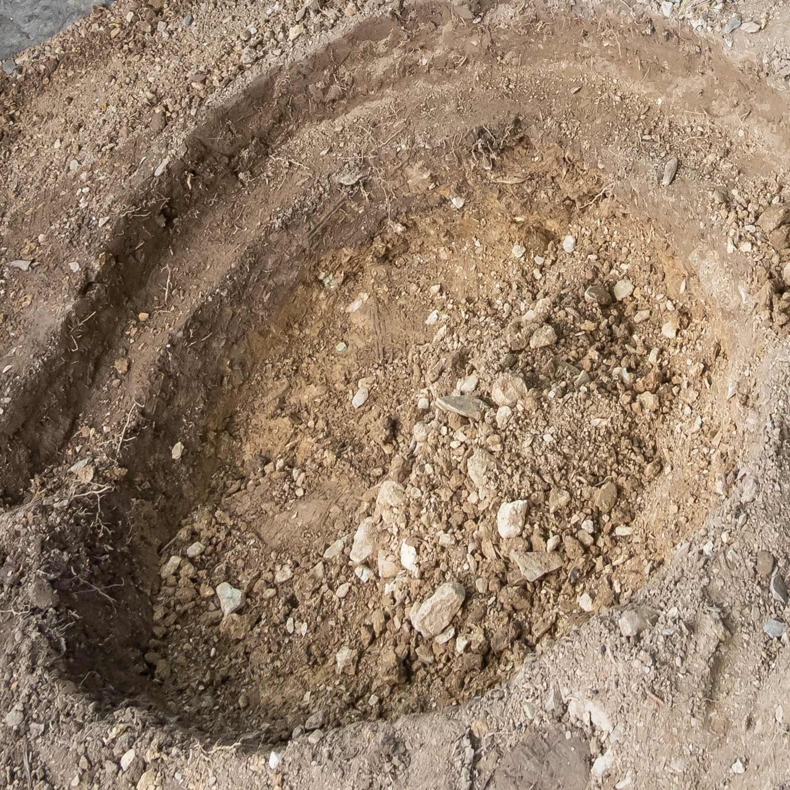 excavated hole for VEVOR pond liner installation, showcasing prepared ground and soil layers.